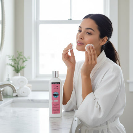 Tia's Treasure Collections Clear Essence Exclusive Glow Tonic bottle on a bathroom counter with a woman applying it.