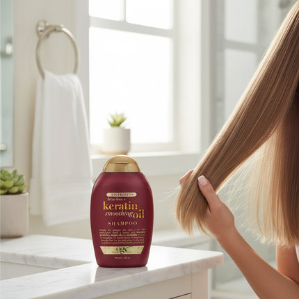 Tia's Treasure Collections Ogx Keratin Smoothing Oil 5-in-1 shampoo bottle on a bathroom vanity with long blonde hair.