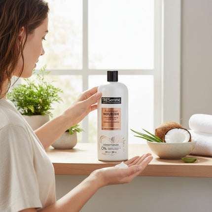 Tia's Treasure Collections Tresemme Botanique Coconut Nourish conditioner bottle held by a woman in a bright room.