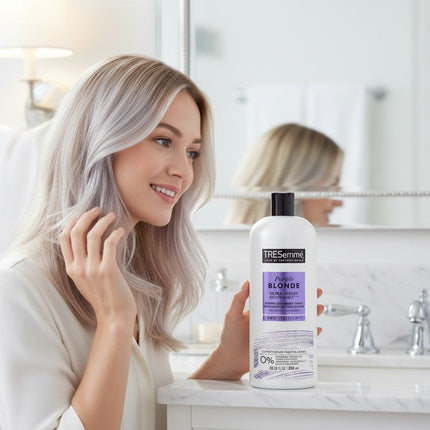 Tia's Treasure Collections Tresemme Purple Blonde conditioner bottle held by a blonde woman in a bright bathroom